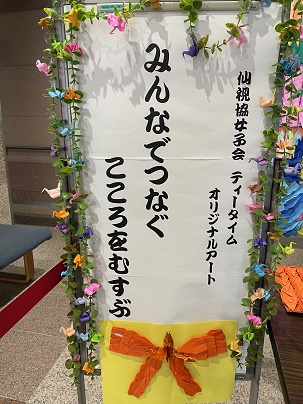 立て看板に仙視協女子会ティータイムオリジナルアートの文字、周りに折り鶴があしらわれている